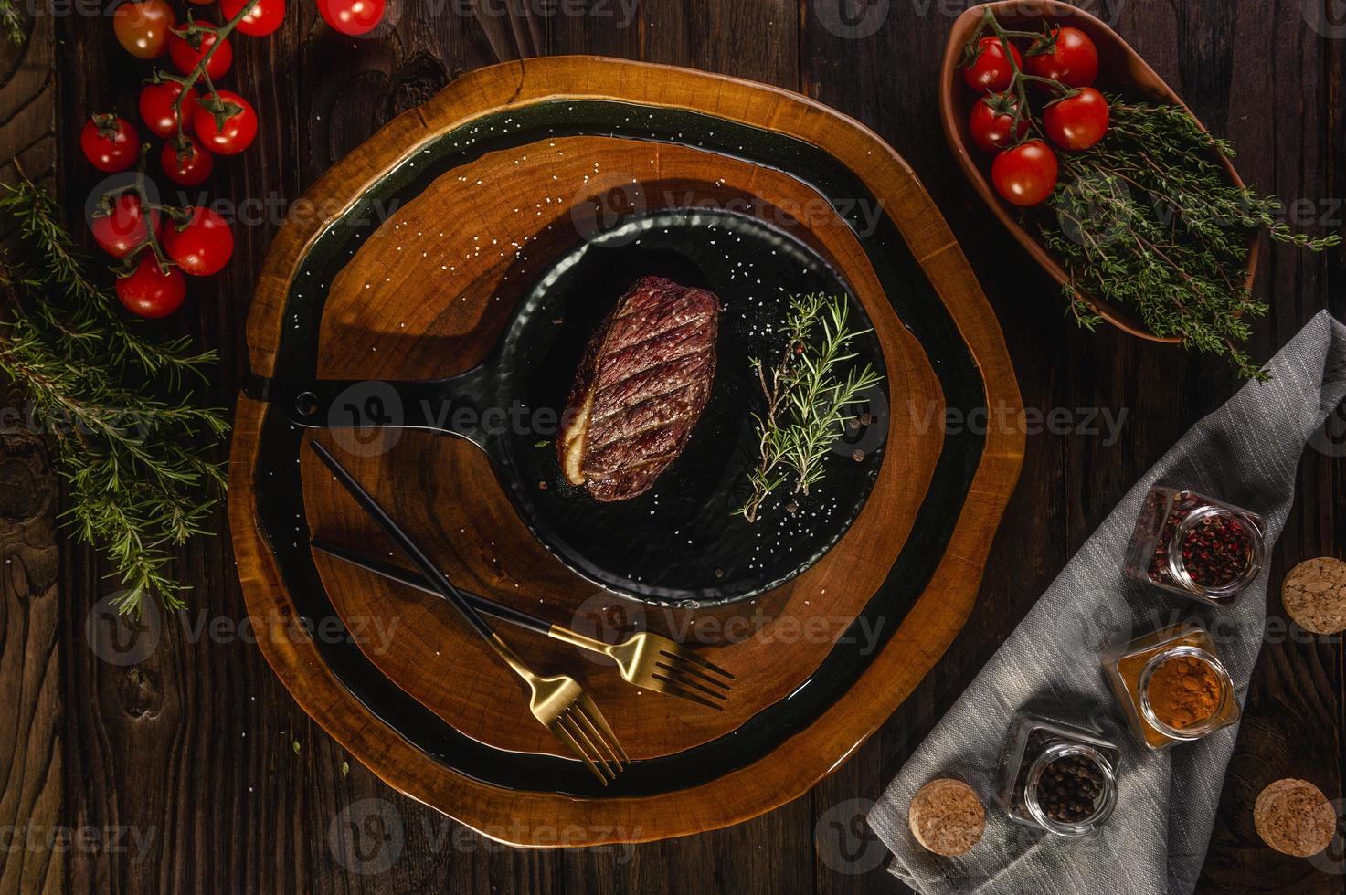 Grilled slice cap rump steak with rosemary branch, golden forks and spices on wooden cutting board - Brazilian picanha - Top view. photo