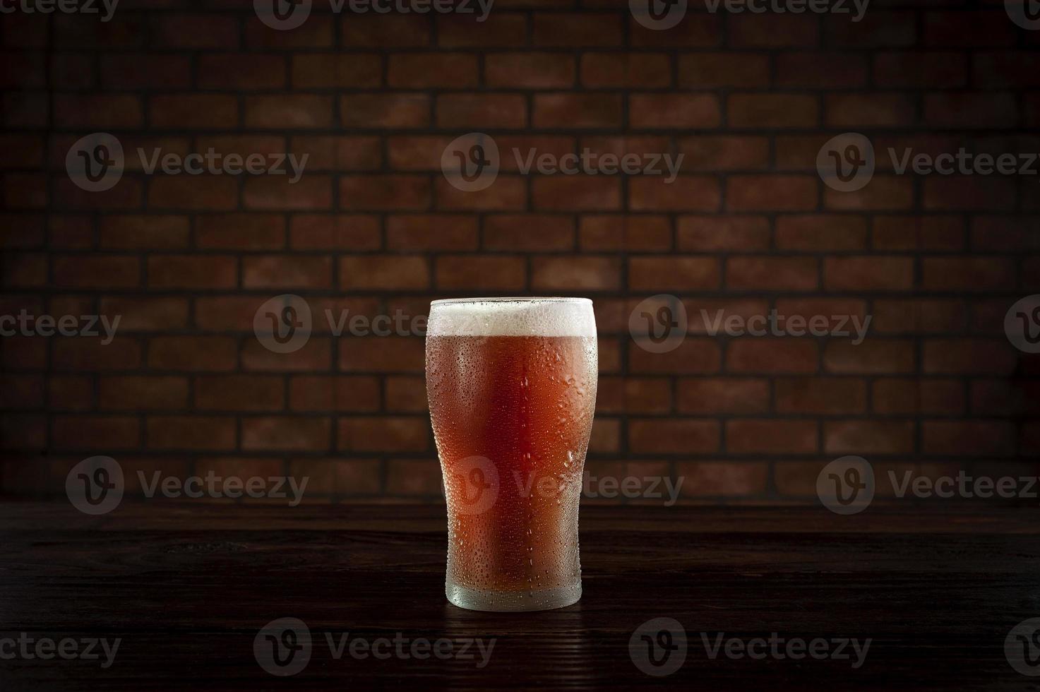 Isolated sweaty glass of refreshing amber ale draft beer with brick wall background. photo