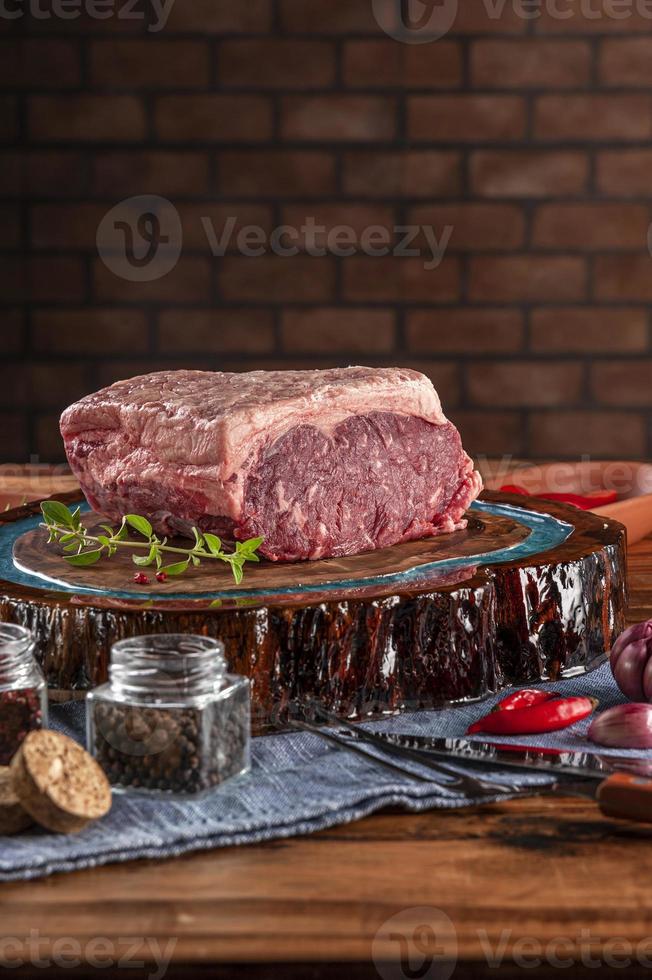 Raw strip loin beef argentine chorizo on a wood resined cutting board with spices. Wooden table with bricks wall background. photo