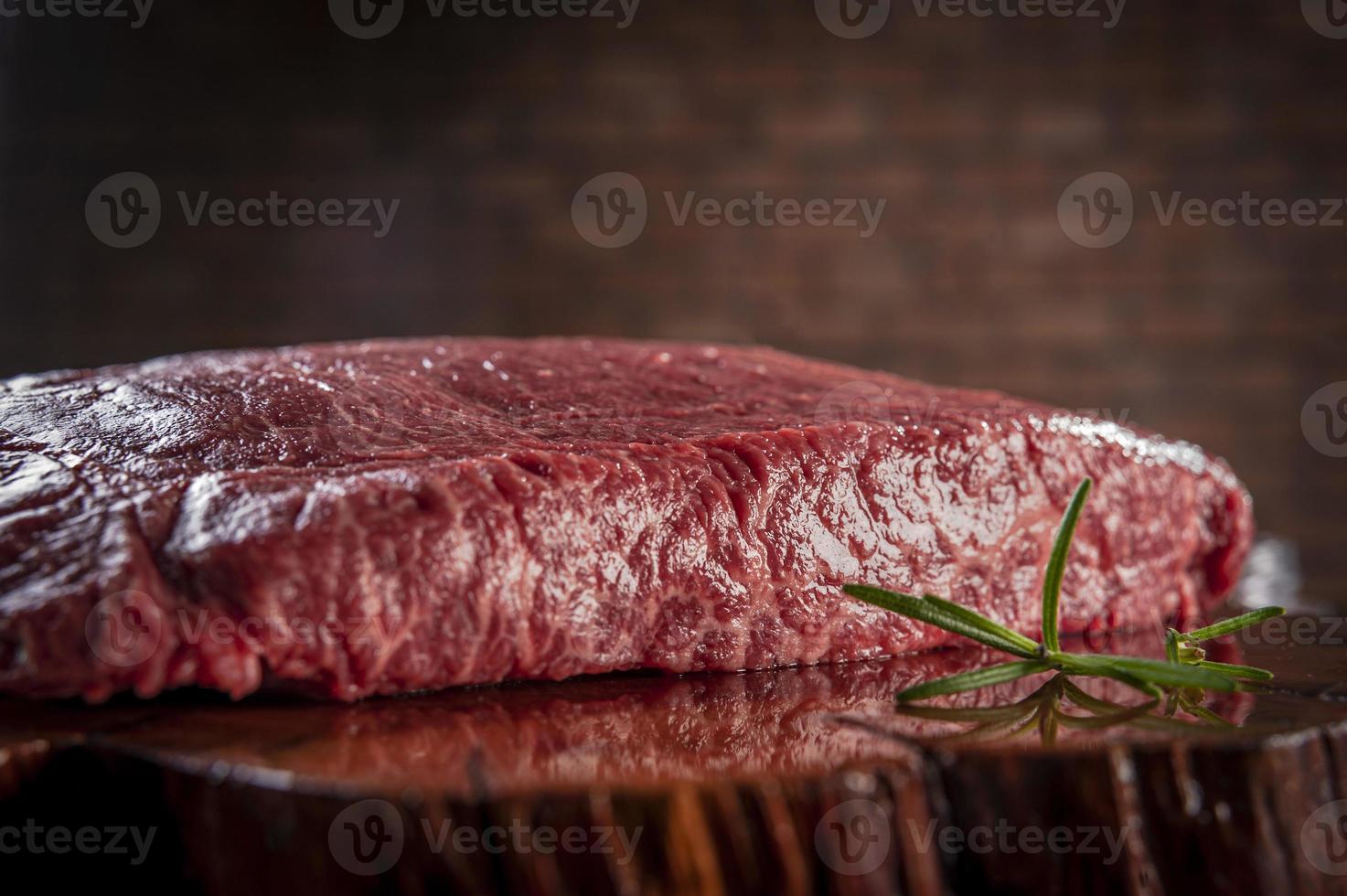 Carne de res de Denver de mármol crudo sobre una tabla de cortar de madera resinada con rama de romero y fondo de pared de ladrillos - primer plano. foto