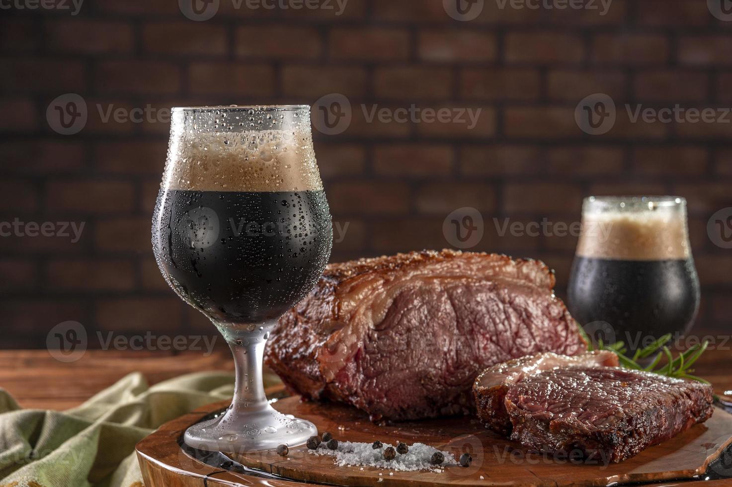 Dos vasos de tulipa sudorosos de cerveza oscura de barril con lomo a la parrilla sobre tabla de cortar de madera. mesa de madera y fondo de pared de ladrillos. foto