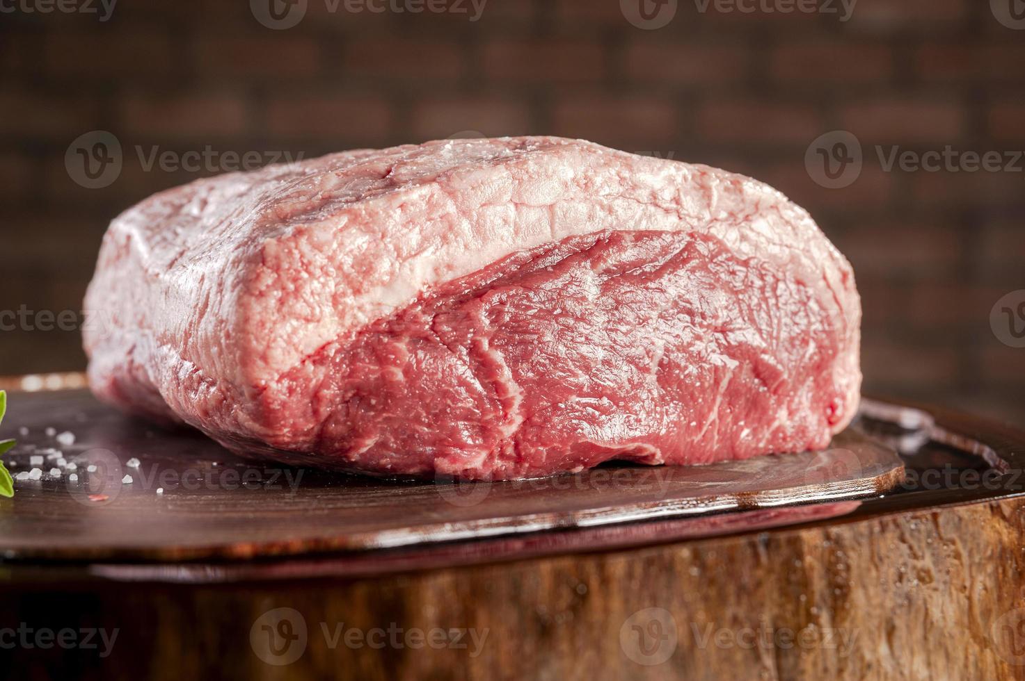 Carne de res de grupa de tapa cruda - picanha brasileña - sobre una tabla de cortar de madera resinada sobre un fondo de pared de ladrillos. foto