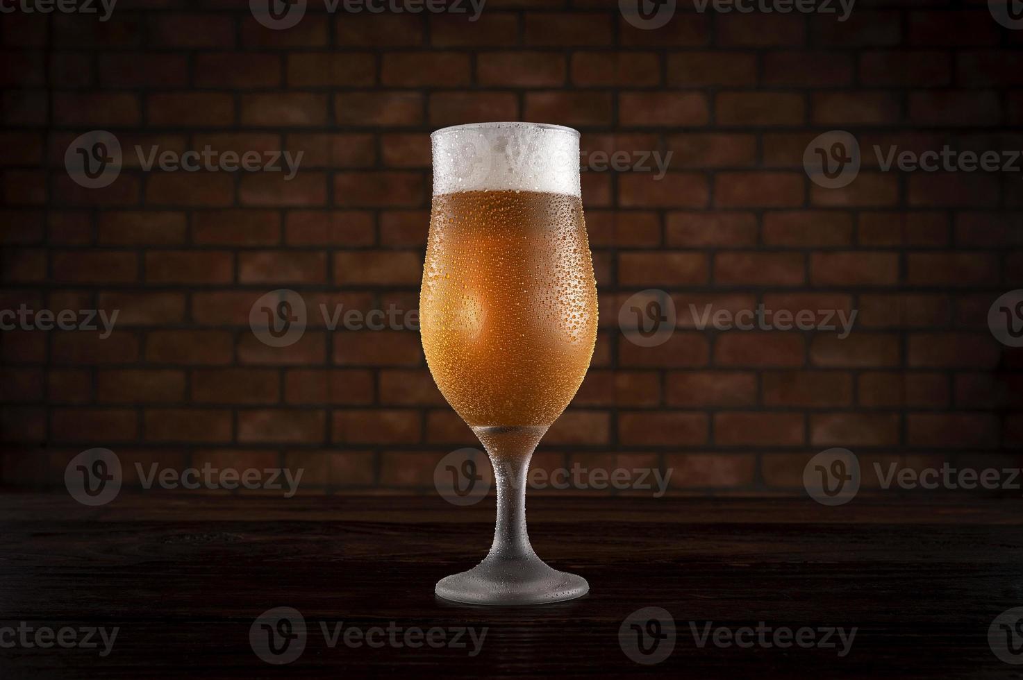 Isolated sweaty tulipa glass of refreshing pilsen draft beer with brick wall background. photo