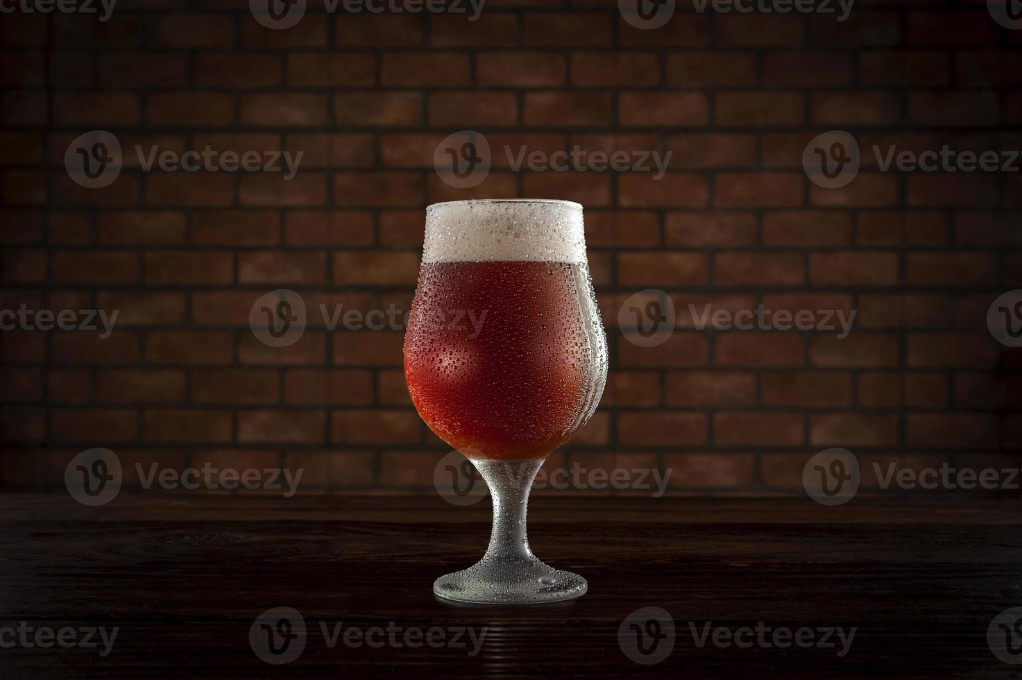 Isolated sweaty tulipa glass of refreshing amber ale draft beer with brick wall background. photo