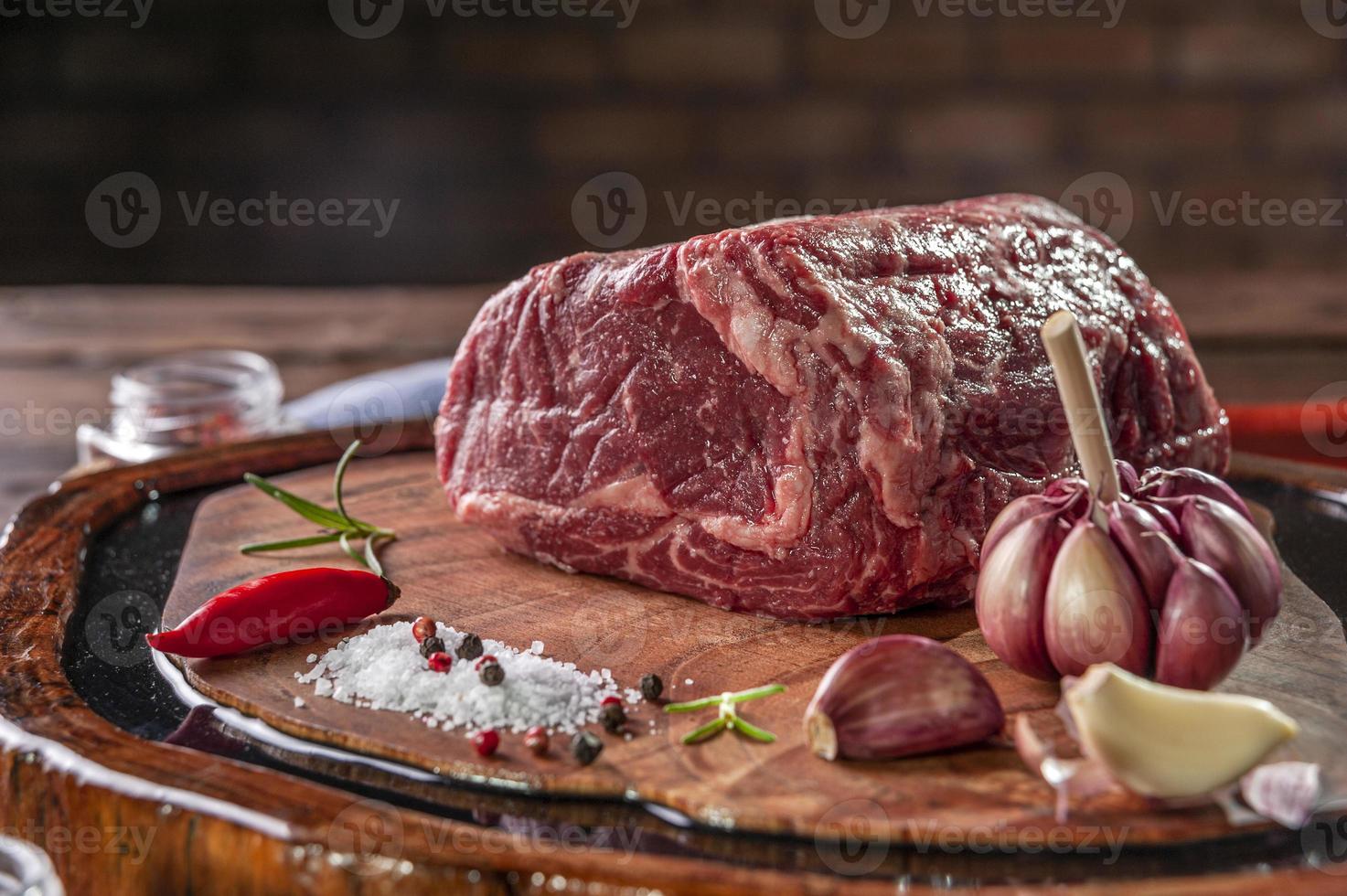 carne cruda de entrecot en una tabla para cortar madera con especias sobre fondo de pared de ladrillos - primer plano. foto