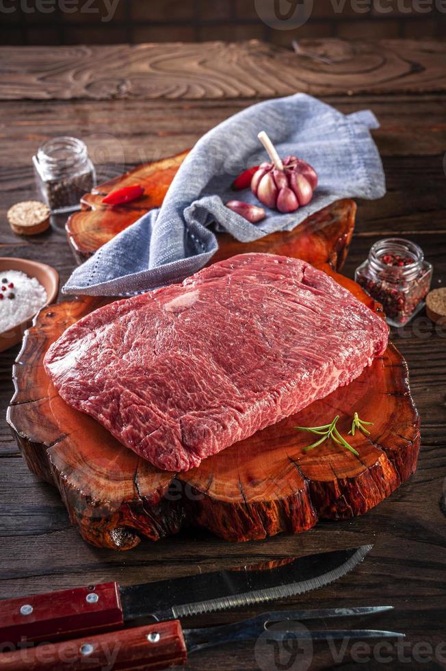 Raw marble denver beef on a wood resined cutting board with spices and barbecue fork and knife. photo