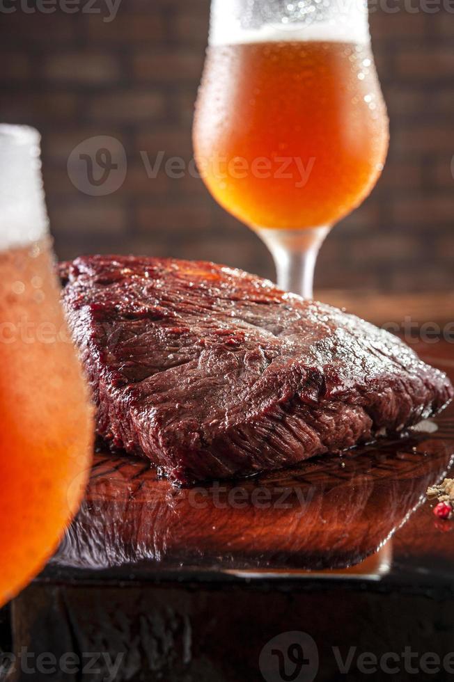 Filete de Denver a la parrilla sobre tabla de cortar de madera con vasos tulipa sudorosos de cerveza de barril. carne de vacuno de mármol. foto