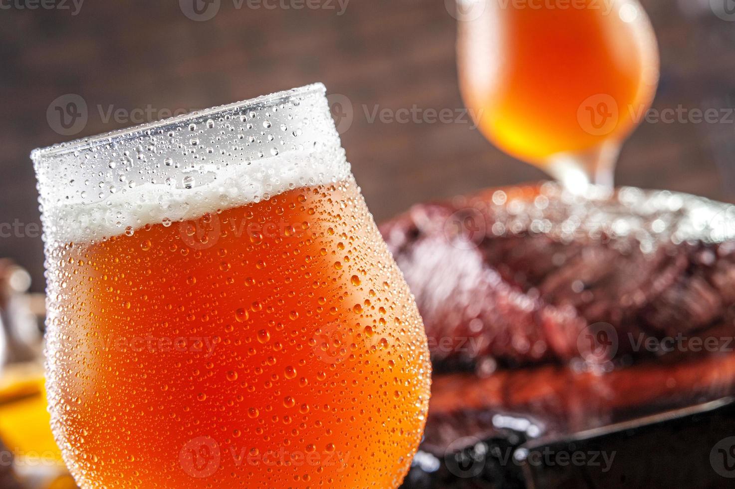 Tulipa fría sudorosa vasos de cerveza de barril ale con bistec de Denver a la parrilla sobre tabla de cortar de madera - primer plano. foto