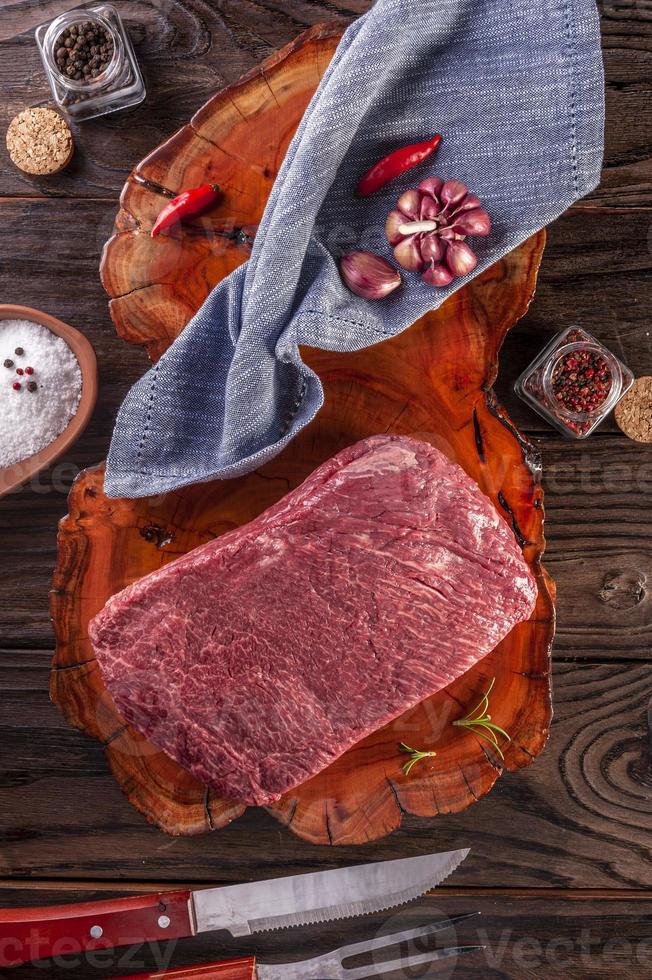 Carne de res de Denver de mármol crudo sobre una tabla de cortar de madera resinada con especias y tenedor y cuchillo de barbacoa - vista superior. foto
