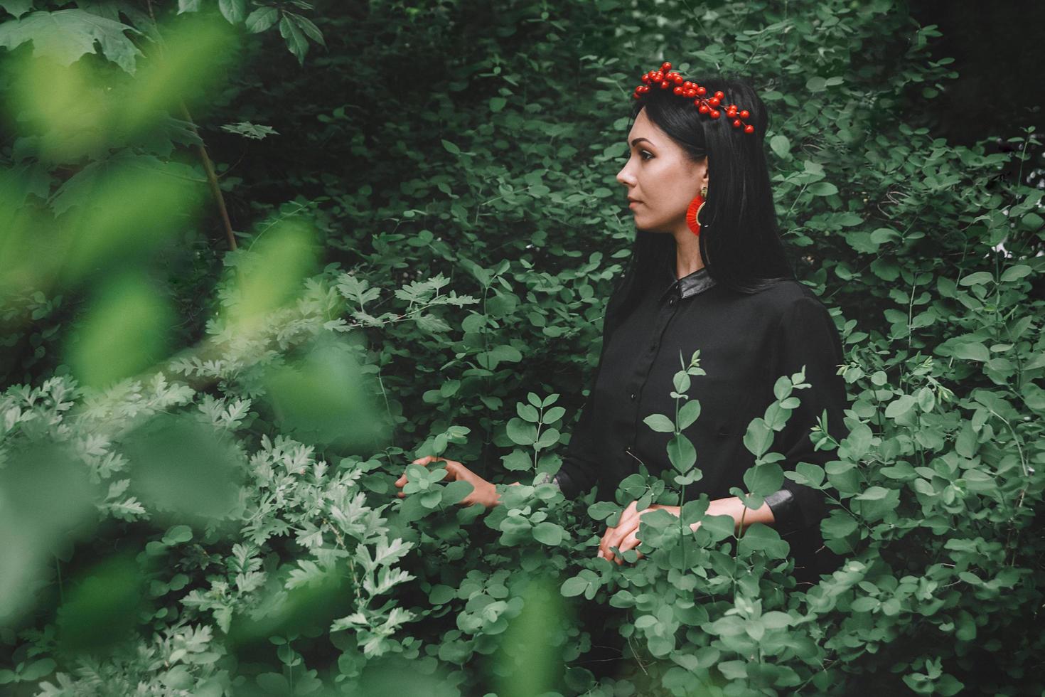 hermosa chica en vestido negro y adornos rojos el fondo del bosque. espacio para su mensaje de texto o contenido promocional foto