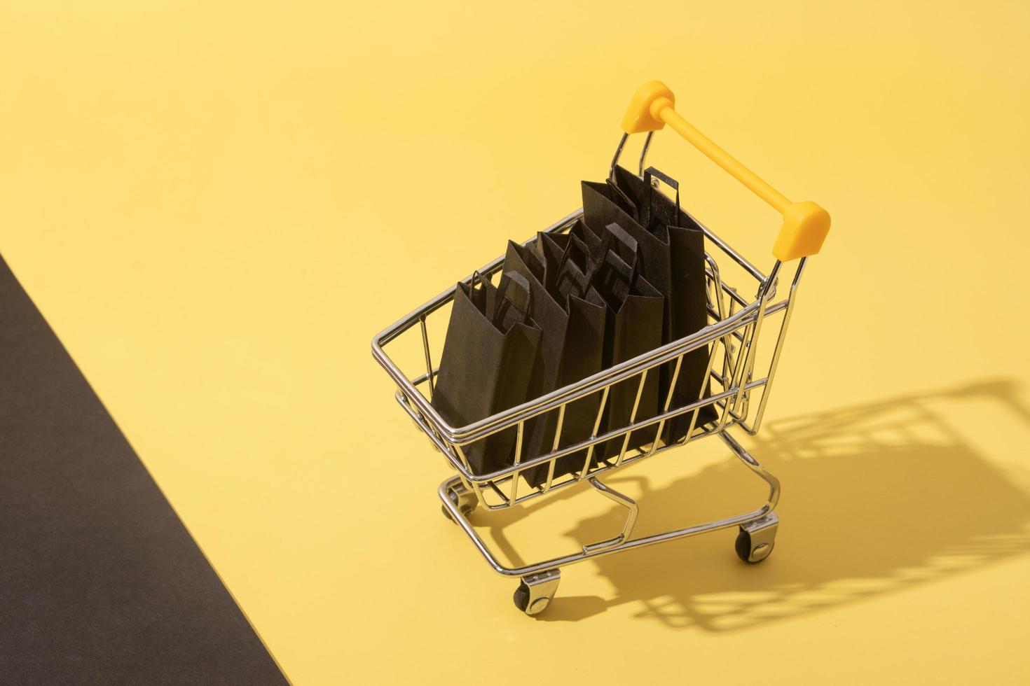 Carro de supermercado en miniatura con bolsas de la compra en venta de viernes negro sobre fondo amarillo foto