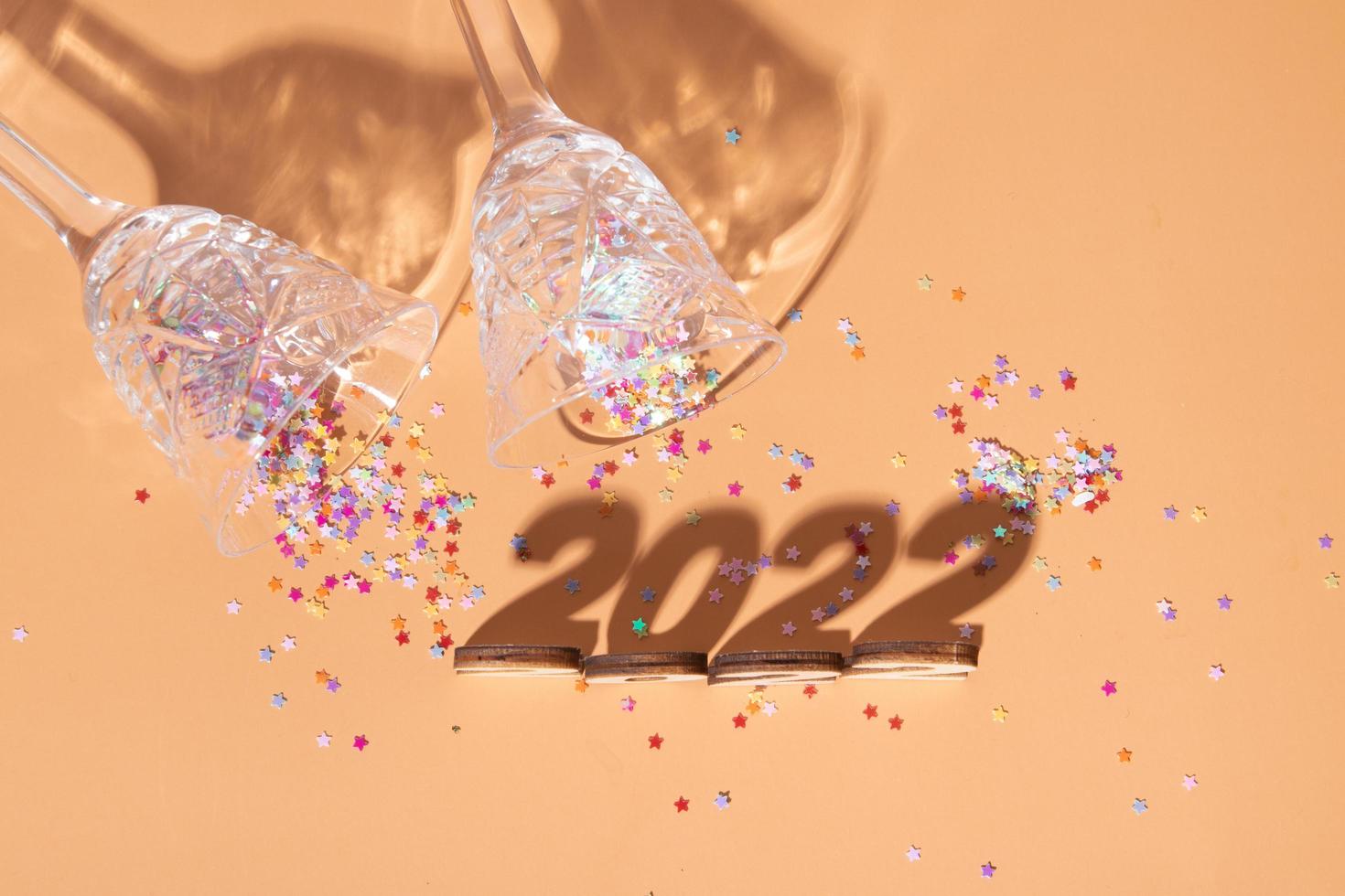 Festive new year flat lay with numbers 2022 and hard shadows with glasses and shiny decor photo