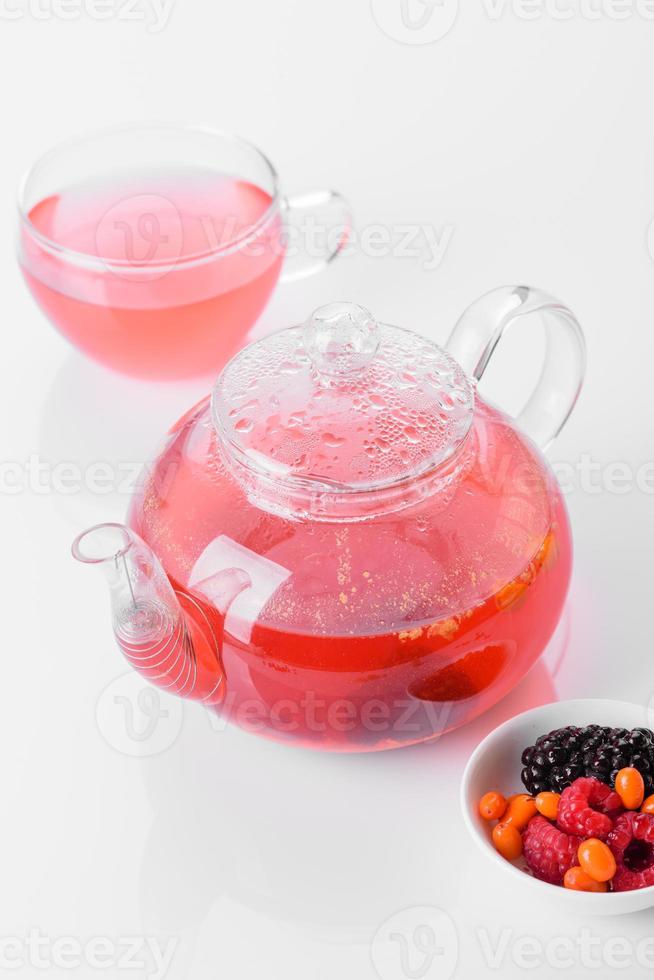 Delicious tea of berries and fruits in a beautiful glass teapot on a white background with reflection photo