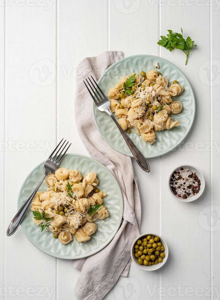 Pasta radiatori con salsa bechamel con guisantes, queso y perejil en placa de color menta sobre fondo de madera foto