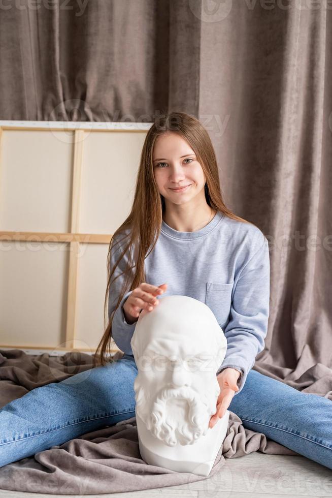 Joven artista femenina sentada en su estudio con el lienzo y la cabeza de Sócrates de yeso foto