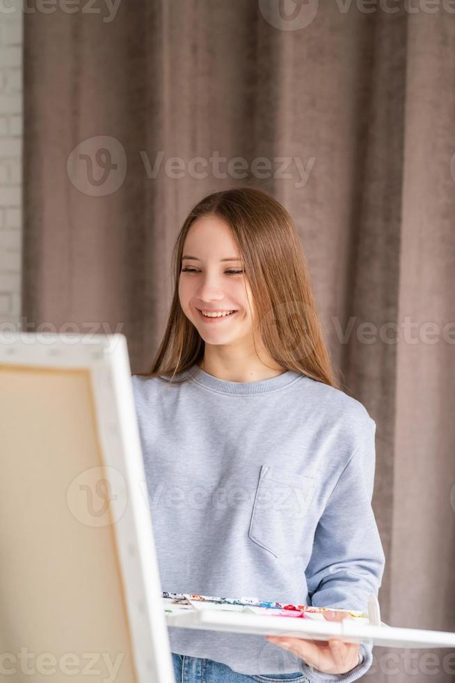 Young female artist painting on the canvas in the studio holding a brush and a palette with watercolors photo