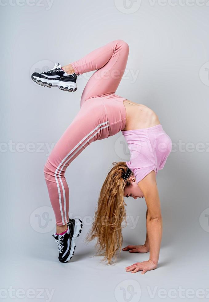 Mujer acróbata vistiendo ropa deportiva rosa trabajando en el estudio aislado sobre fondo gris foto