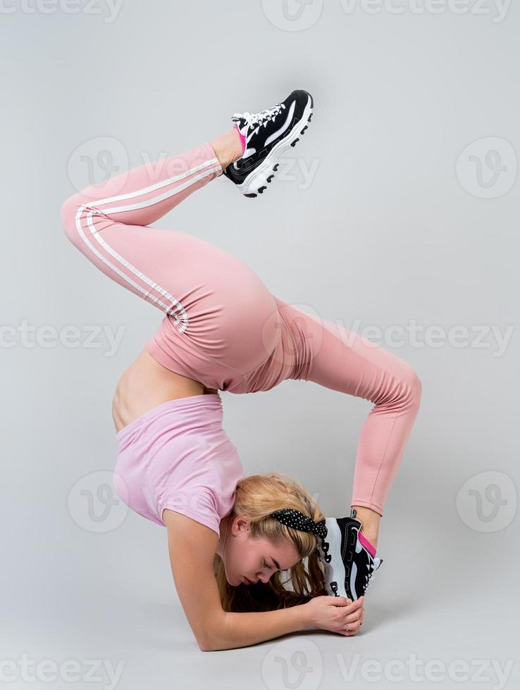 Sonriente mujer acróbata vistiendo ropa deportiva rosa trabajando en el estudio aislado sobre fondo gris foto