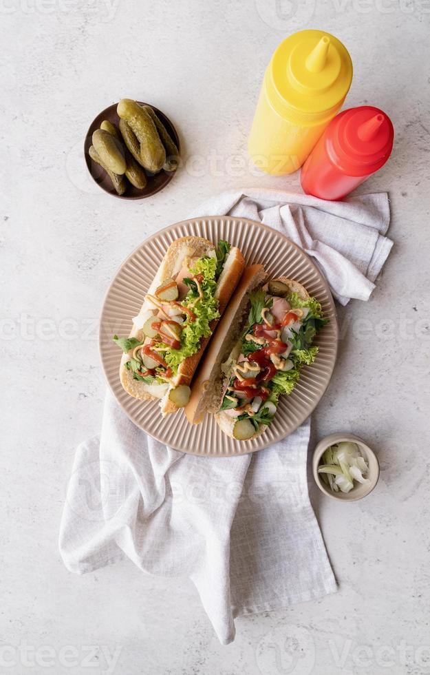 Hot dog with sausage, letuce, cucumber and onion on beige plate on concrete background photo