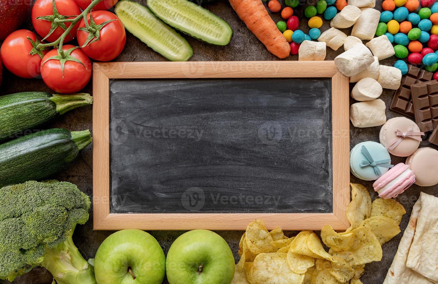 frutas y verduras vs dulces y papas fritas alrededor de la vista superior de la pizarra en blanco plano foto