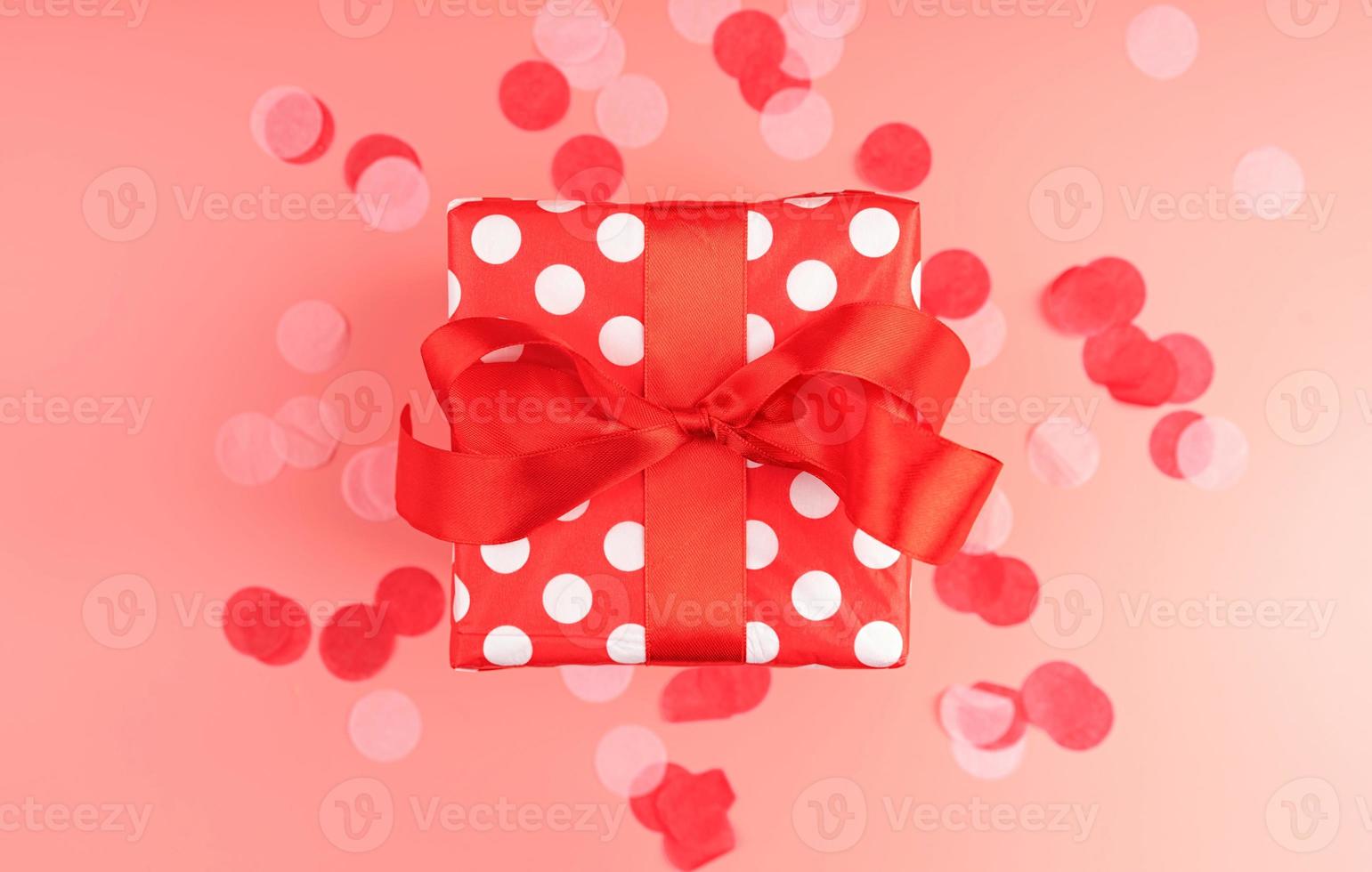 Single red gift box with red confetti on pink background top view photo