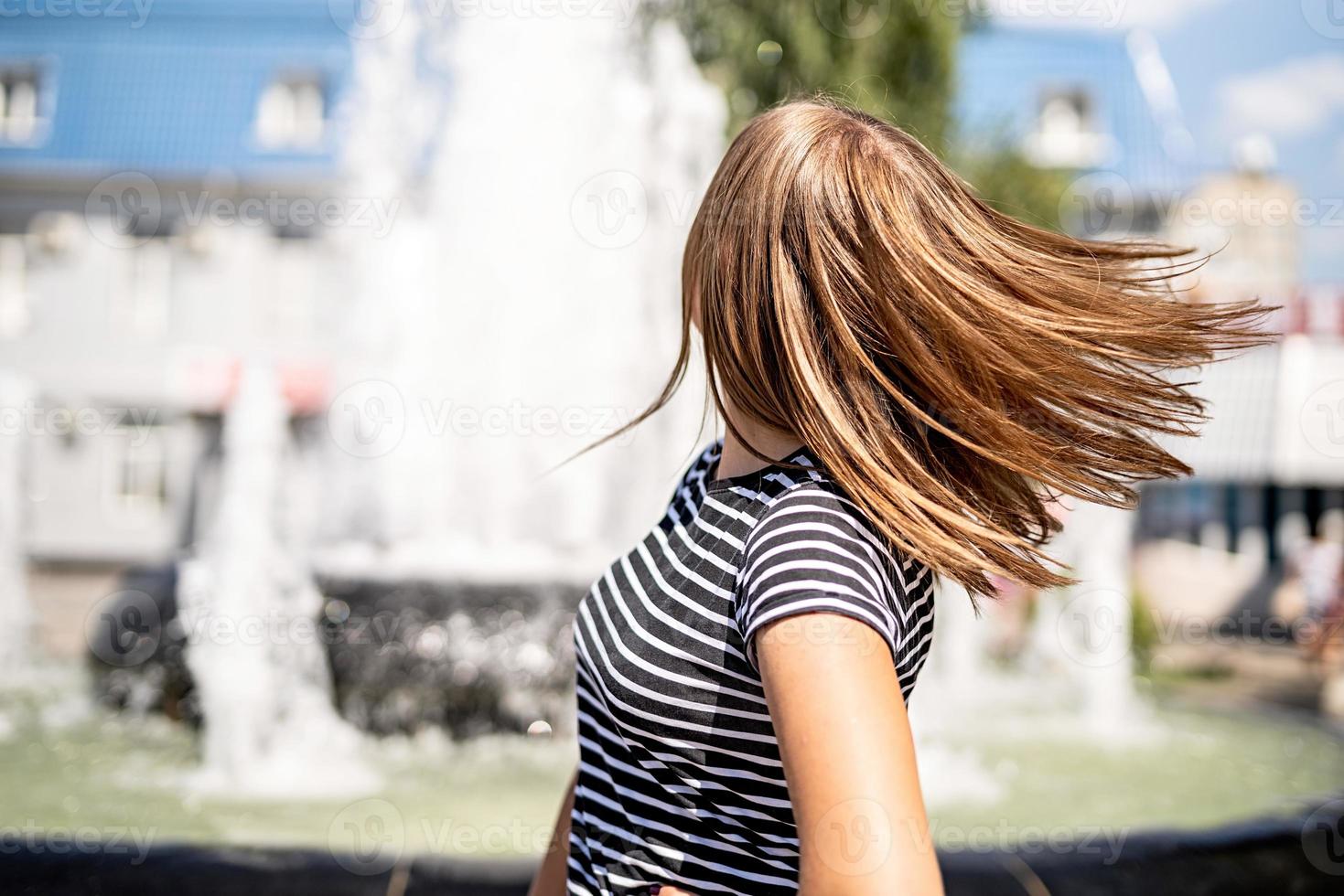 Hermosa mujer en ropa casual divirtiéndose dando vueltas en el fondo de la fuente urbana en un día soleado foto