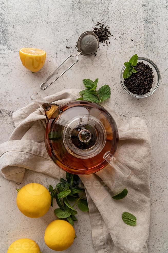 teapot with black tea decorated with mint leaves, lemons and dry tea leaves top view flat lay photo