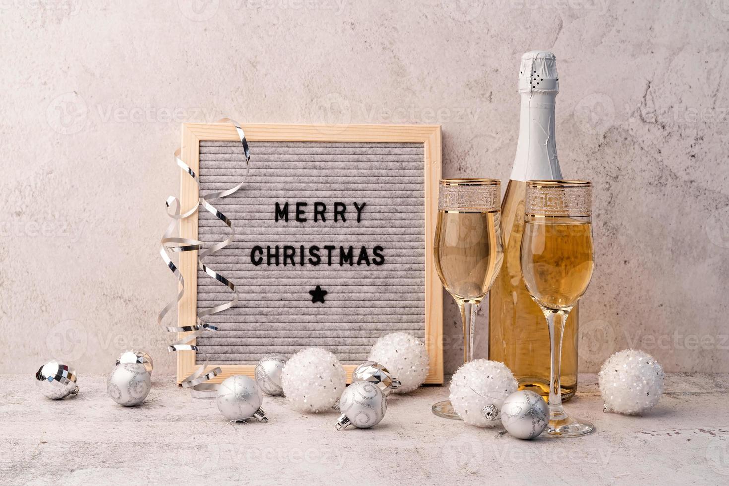 Cartón de fieltro feliz navidad en la mesa con copas de champán y botella foto
