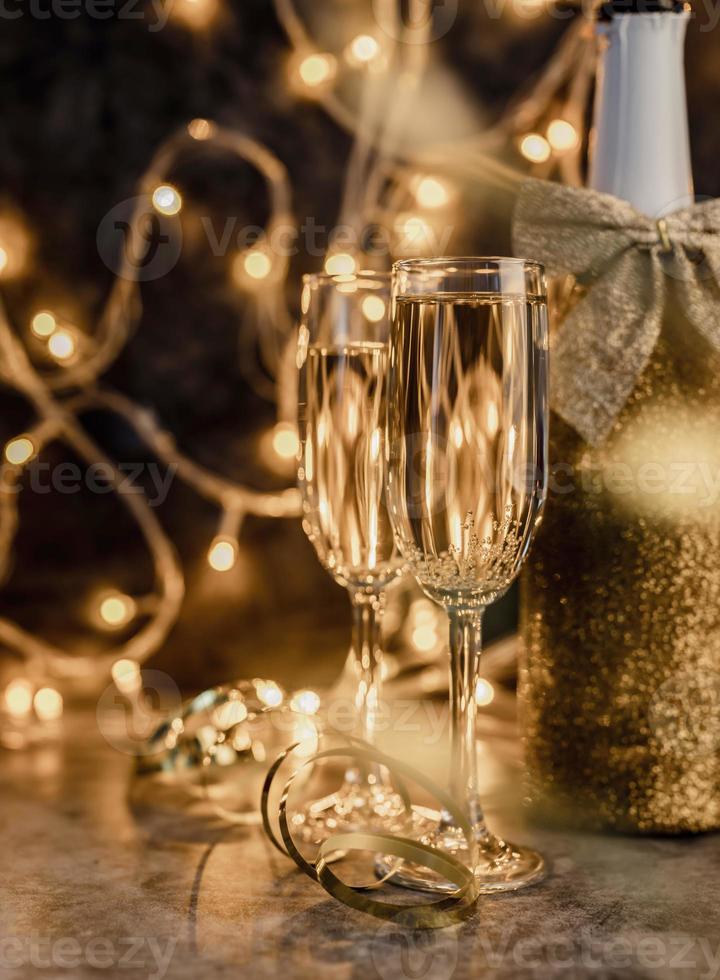 two champagne flute with shiny bottle on dark background with lights photo