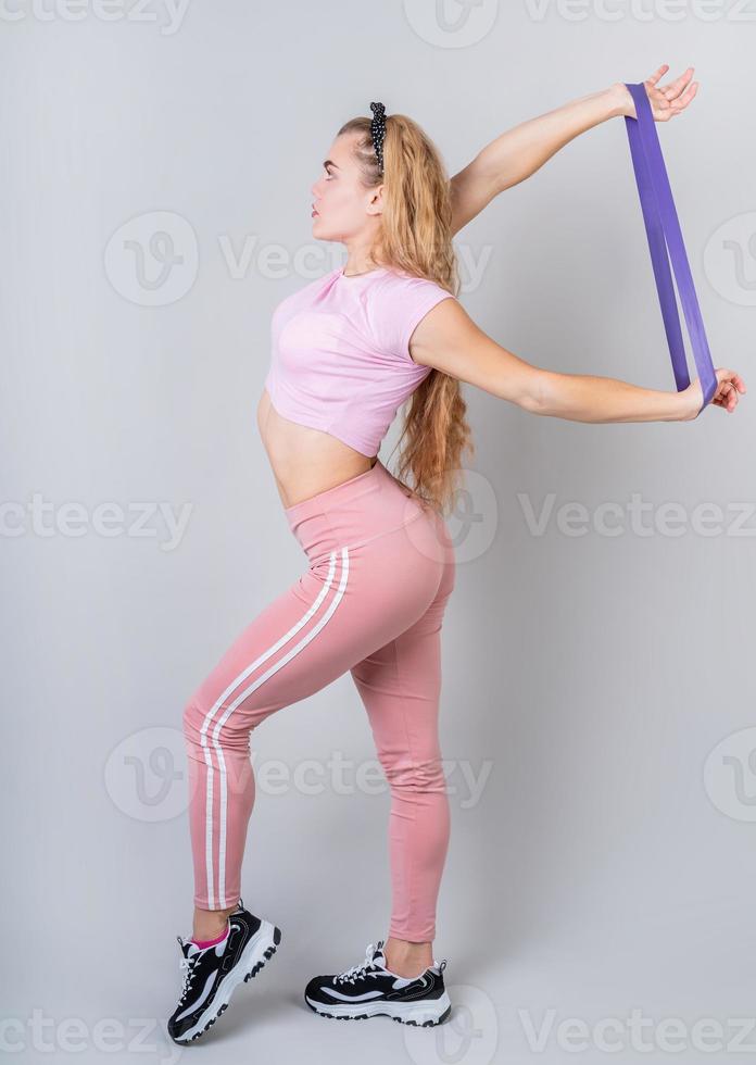 Acrobat woman wearing pink sportswear working out in the studio using rubber resistance band isolated photo
