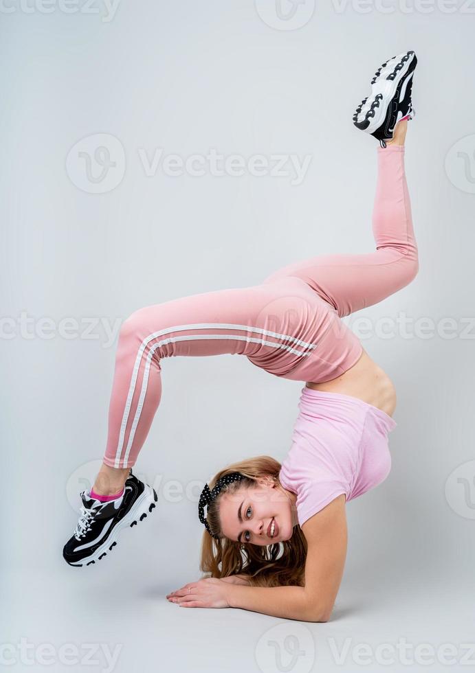 Sonriente mujer acróbata vistiendo ropa deportiva rosa trabajando en el estudio aislado sobre fondo gris foto