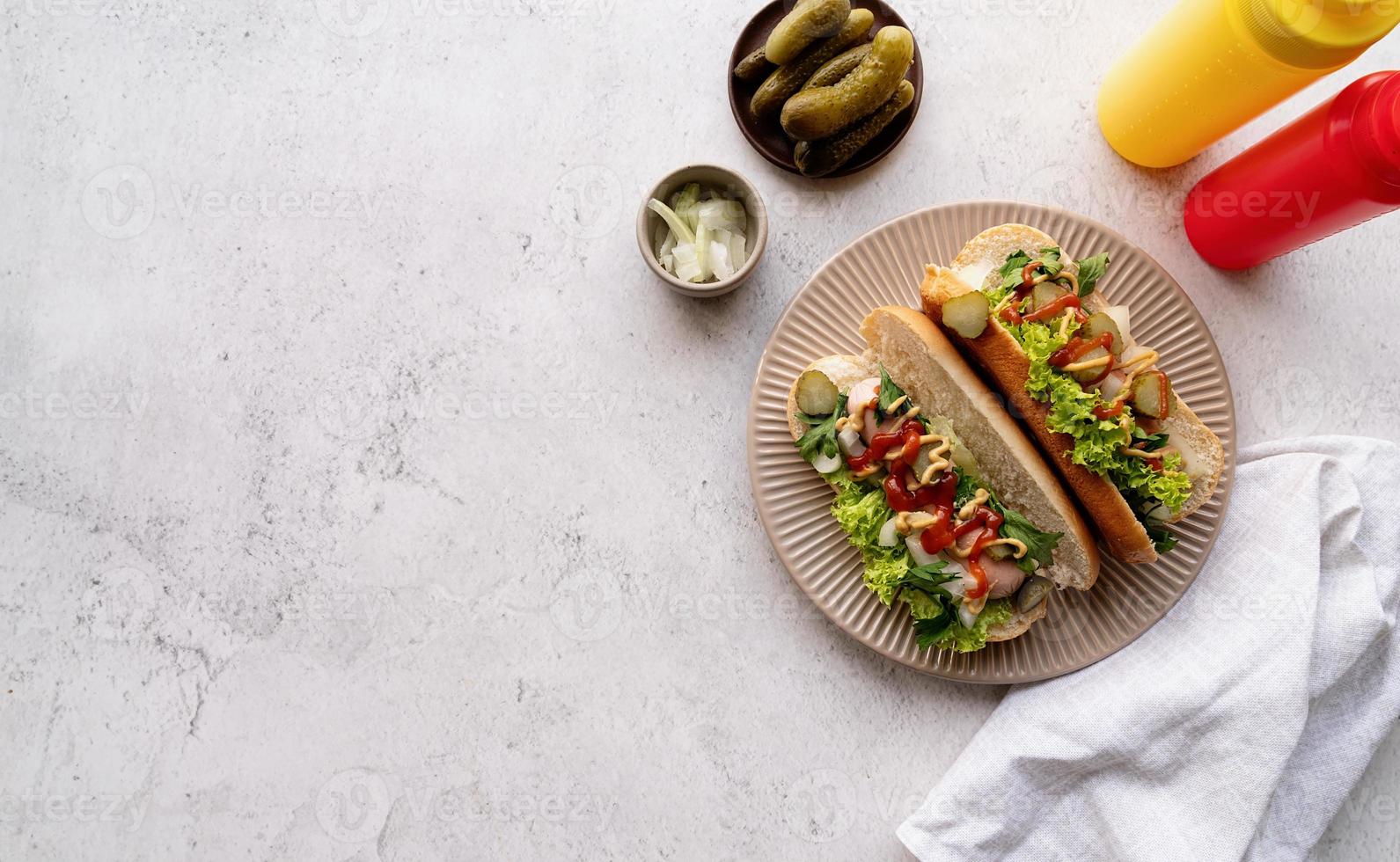 Hot dog with sausage, letuce, cucumber and onion on beige plate on concrete background photo