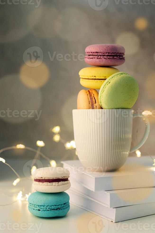 white coffee cup filled with macaroons on the table, fairy lights and bokeh background photo