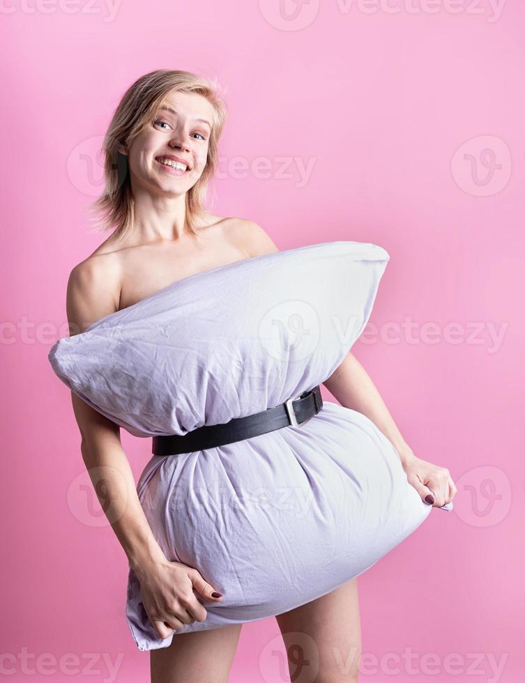 young beautiful woman dressed in pillow smiling isolated on pink background photo