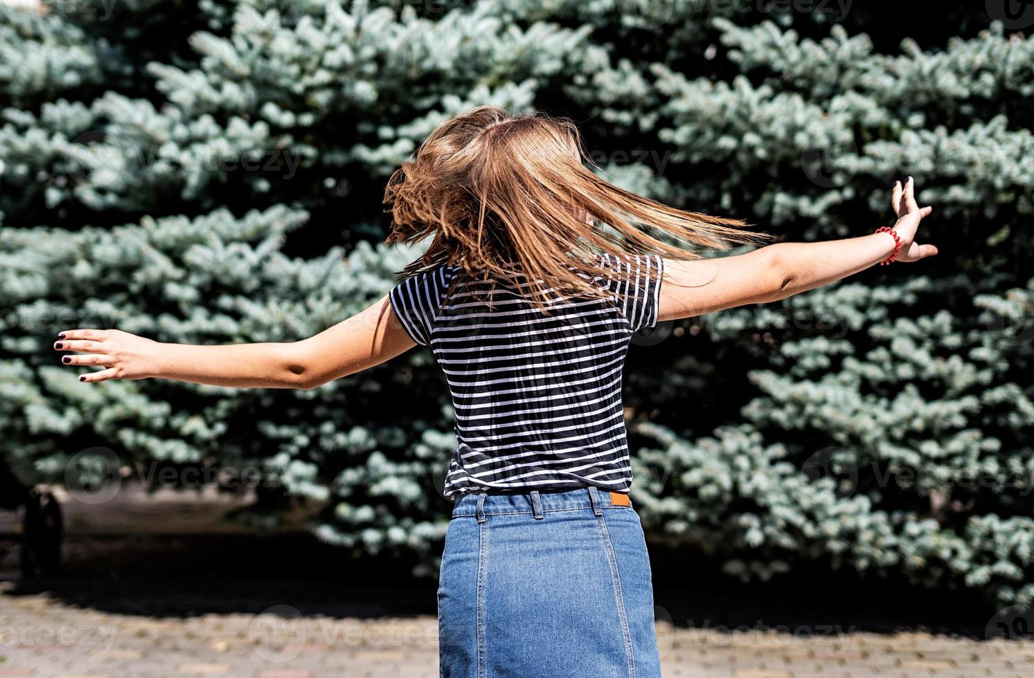 young pretty caucasian woman in casual clothes having fun turning around on fir trees background in the park photo