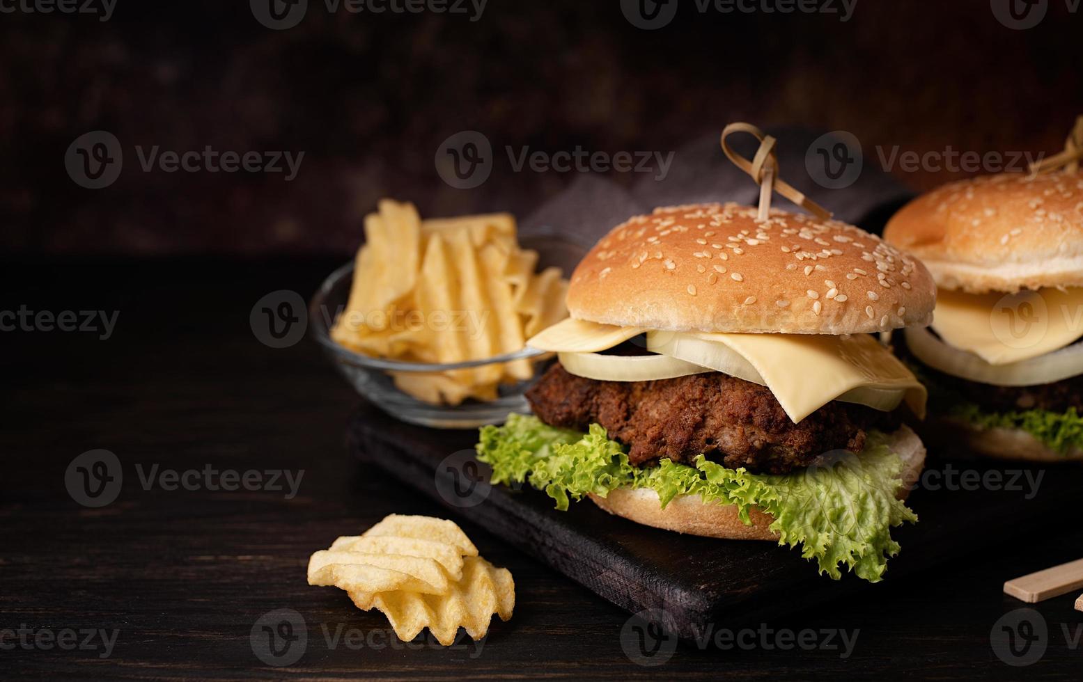 Un conjunto de deliciosas hamburguesas caseras de ternera, cebolla, queso y lechuga sobre un fondo de madera oscura. foto