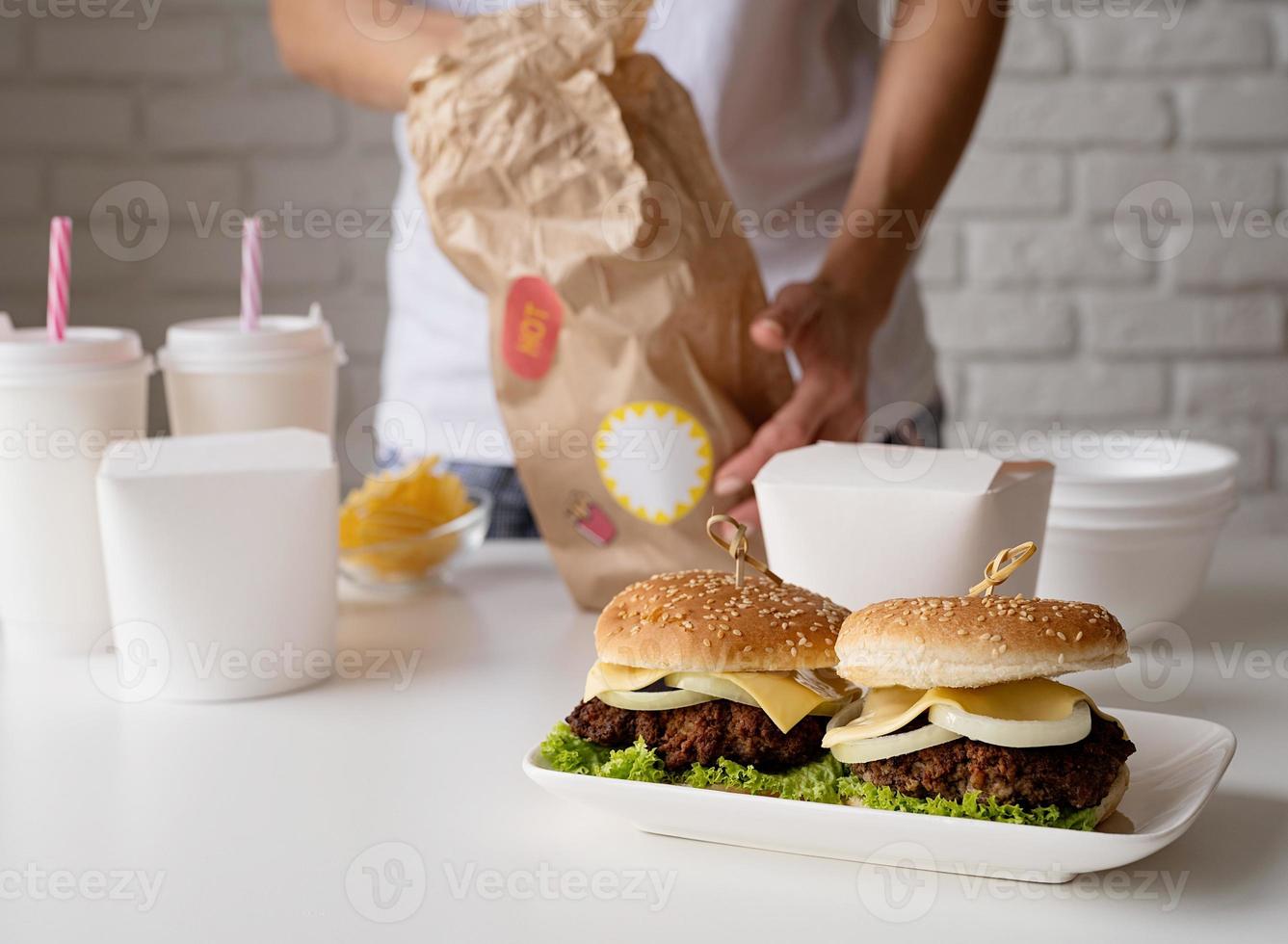 Mujer en ropa de casa desembalaje de comida a domicilio con hamburguesas, cajas de fideos y bebidas foto