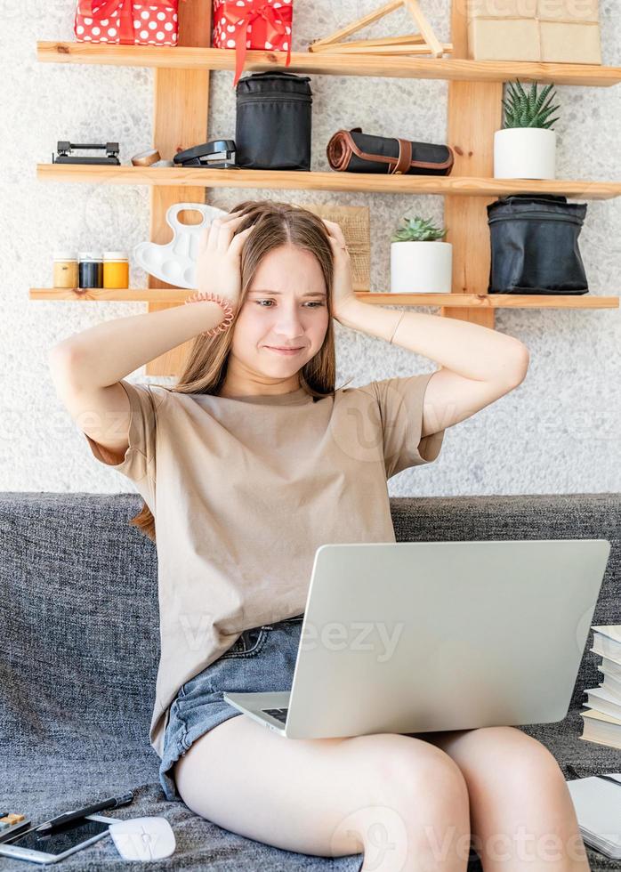 Conmocionada jovencita estudiando usando su computadora portátil en casa foto