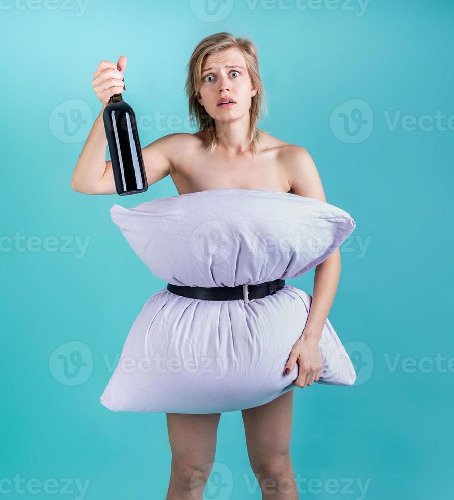 Desperate woman in pillowdress holding a wine bottle isolated on blue background photo