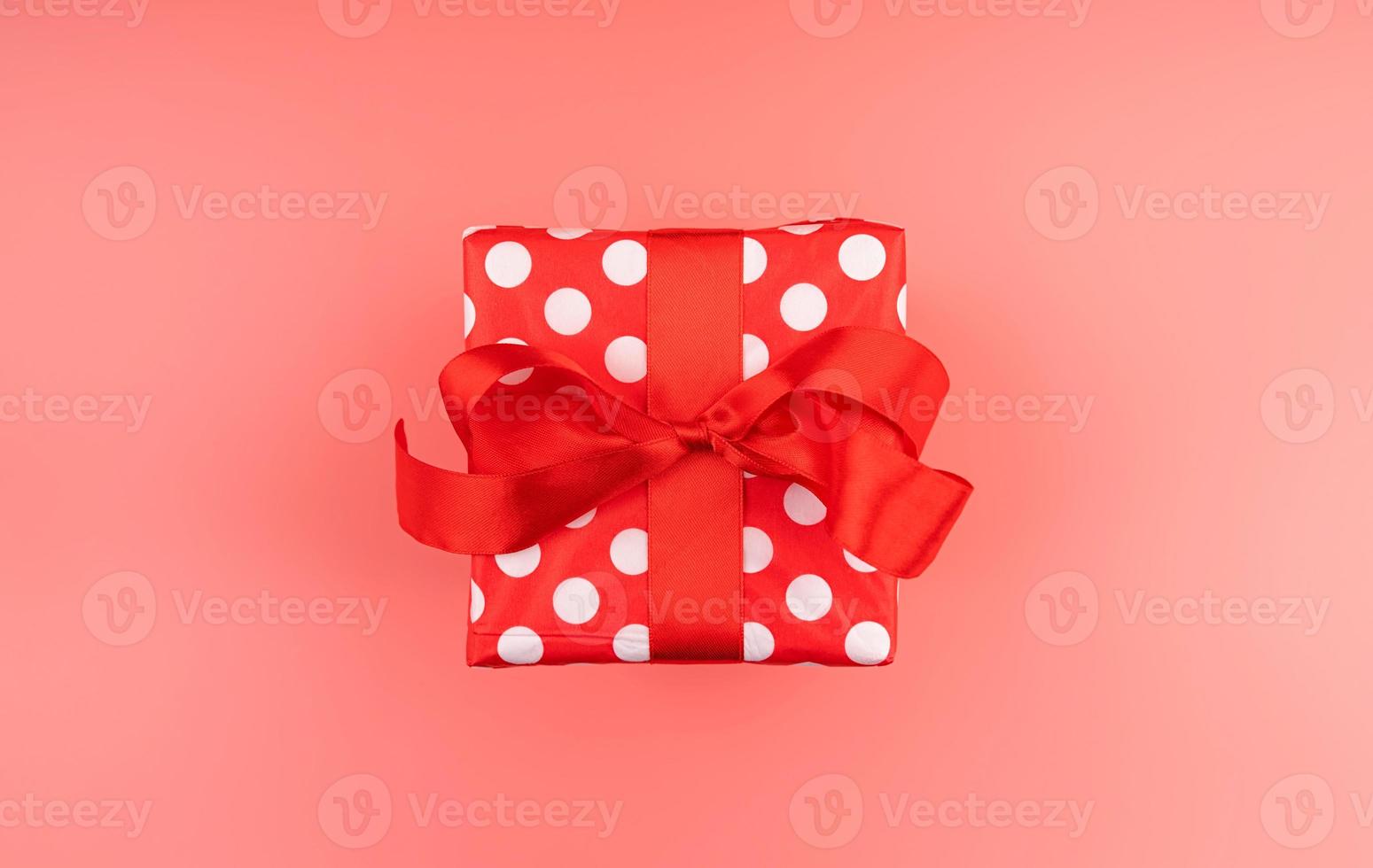 Single red gift box with red ribbon on pink background top view photo