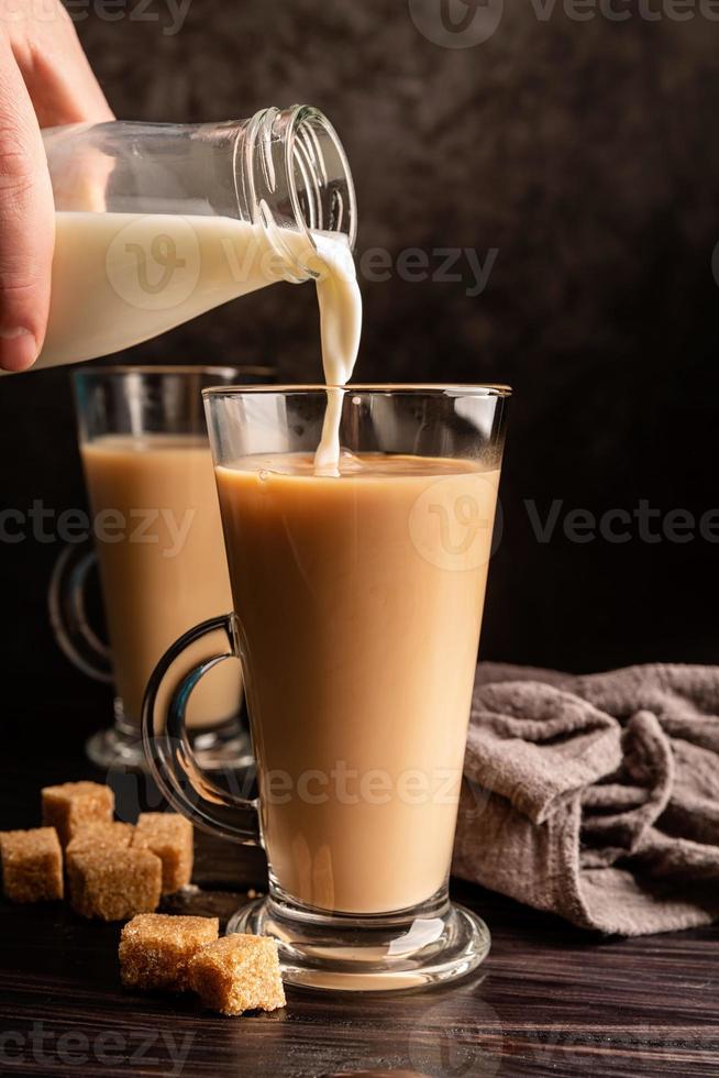Mano masculina vertiendo leche en vista frontal de té negro caliente sobre fondo oscuro foto