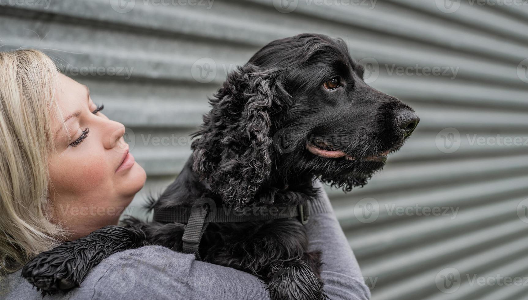Mujer joven sosteniendo su perro cocker spaniel sobre fondo de pared gris exterior foto
