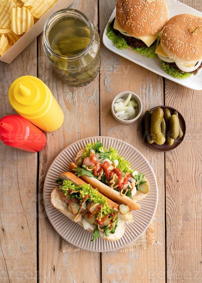 Perrito caliente con salchicha, lechuga, pepino y cebolla en placa beigw sobre fondo de madera foto