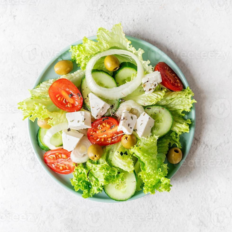 Ensalada griega con queso feta, verduras frescas y aceitunas sobre fondo blanco rústico vista superior orientación cuadrada foto