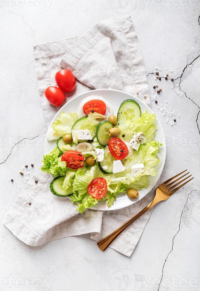 Ensalada griega con queso feta, verduras frescas y aceitunas sobre fondo blanco rústico vista superior foto