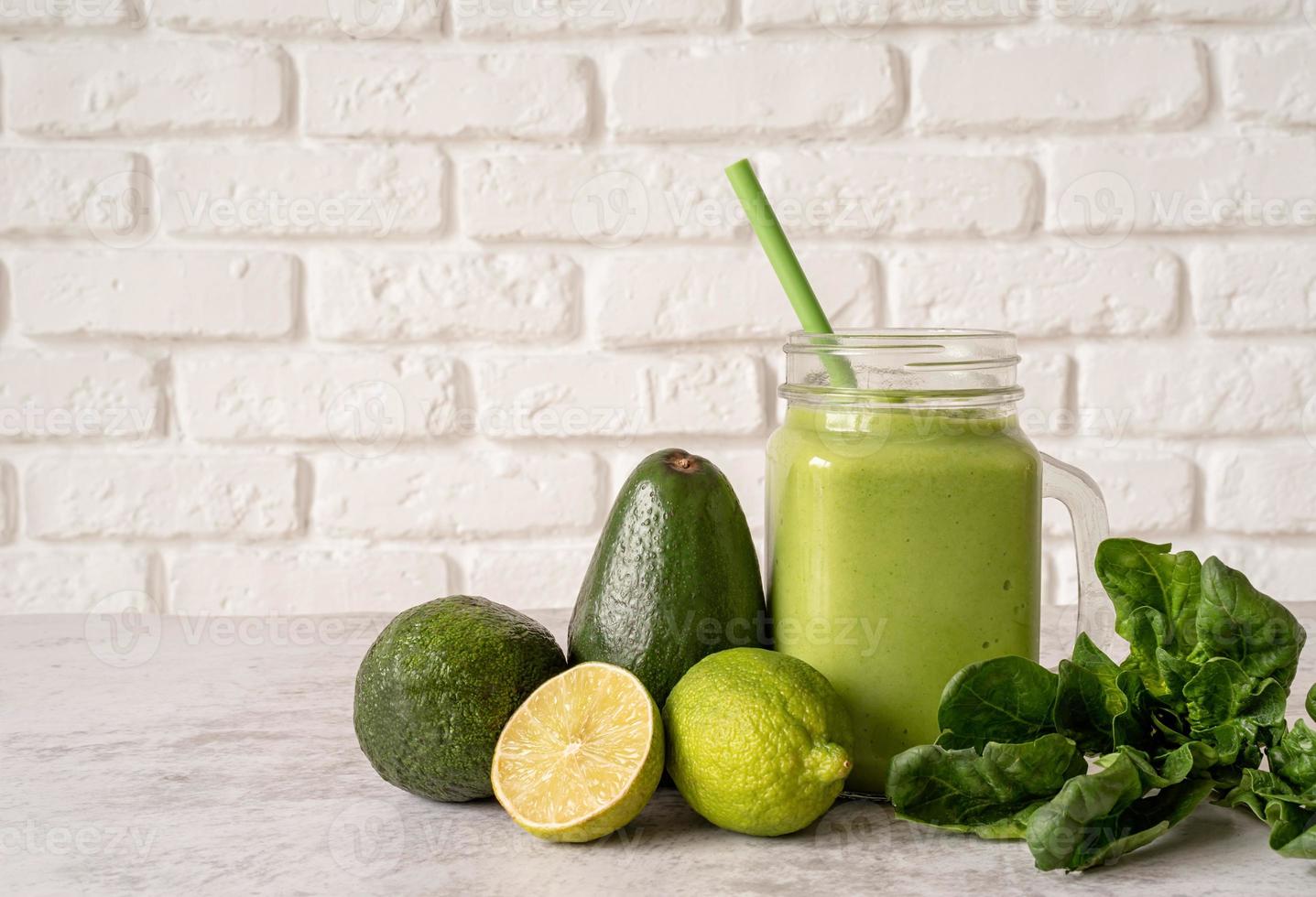 Avocado and spinach smoothie in mason jar front view on white brick wall background photo