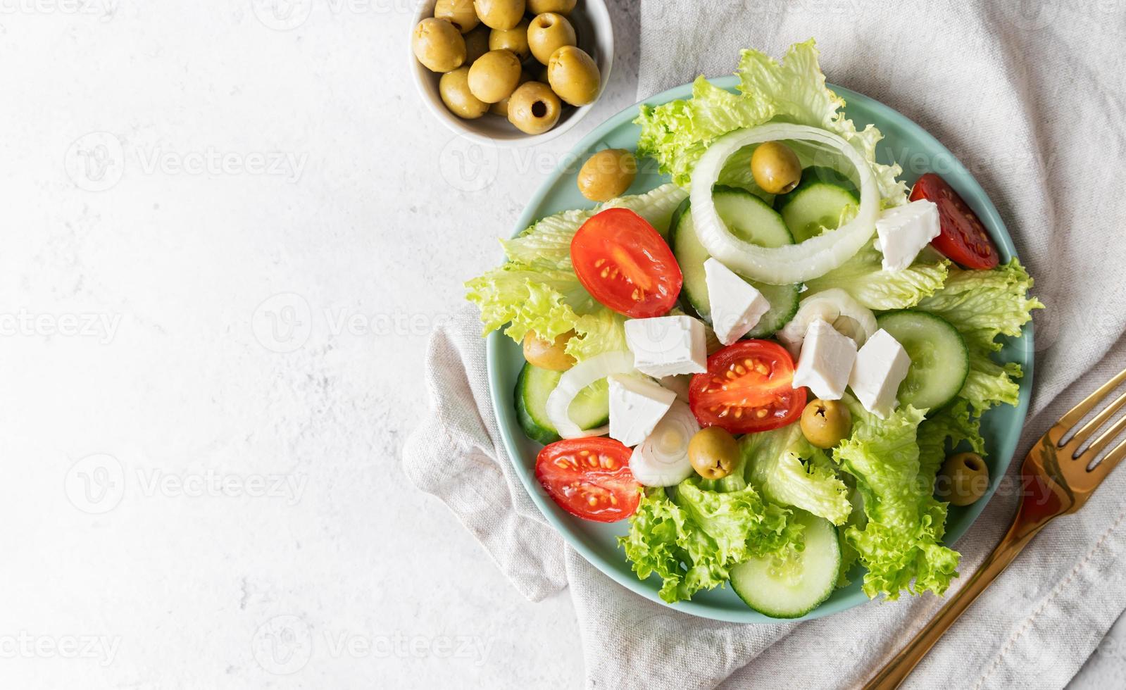 Ensalada griega con queso feta, verduras frescas y aceitunas sobre fondo blanco rústico vista superior con espacio de copia foto
