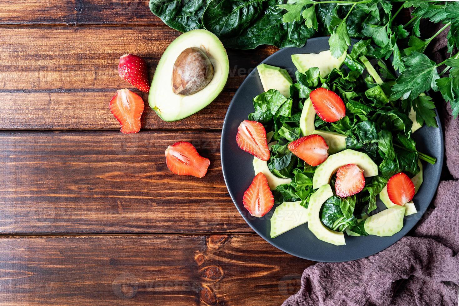 Vista superior de ensalada de aguacate, espinacas y fresas sobre fondo de madera con espacio de copia foto