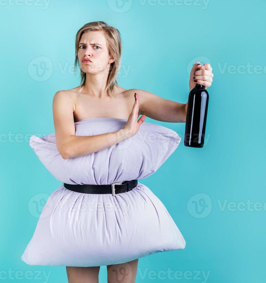 Blonde woman in pillowdress holding a wine bottle showing denying gesture isolated on blue background photo
