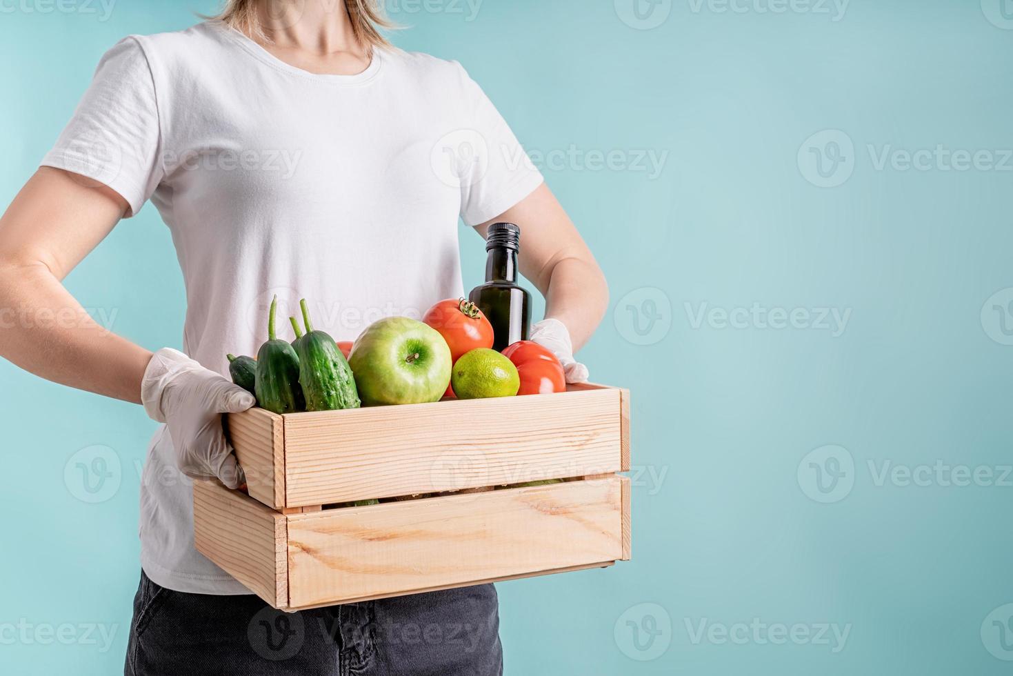 Mujer rubia en guantes sosteniendo una caja de madera llena de verduras con espacio de copia foto